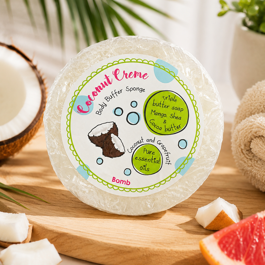 Coconut Creme bath buffer sponge on a wooden board with coconut and grapefruit slices, and plants in the background.