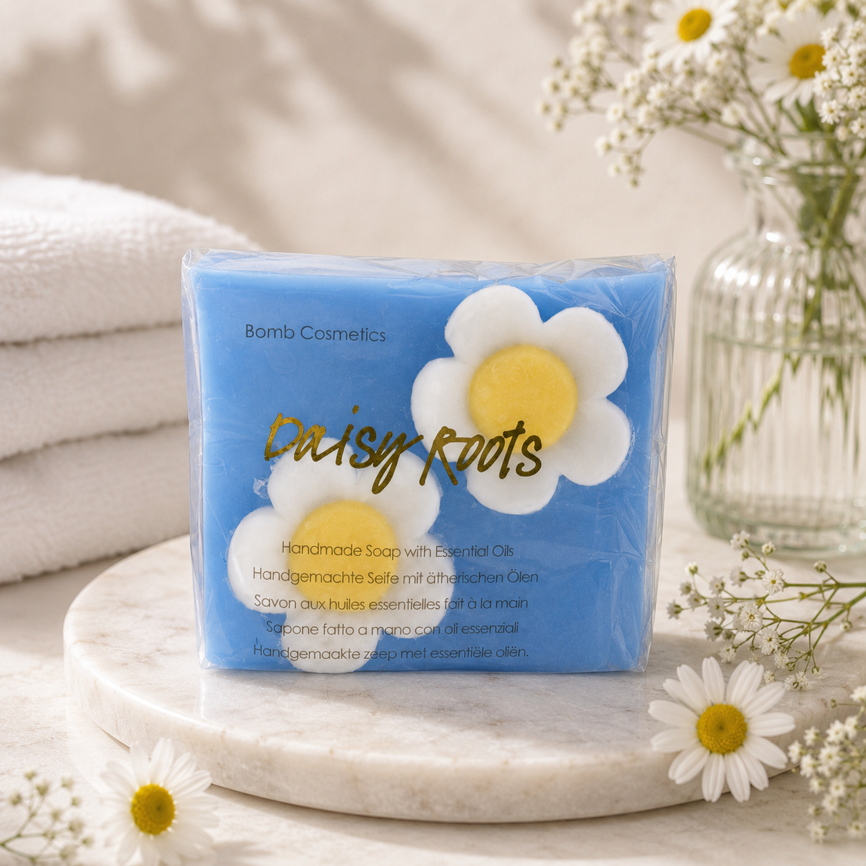 Soap packaging with daisy design on a marble surface with flowers and towels in the background