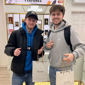 Two people holding Pearl Fragrances bags in Pearl Fragrances with 'Arabian perfumes' display in the background