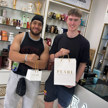 Two men standing in a store holding a 'Pearl fragrances' bag, with store shelves and branding in the background.